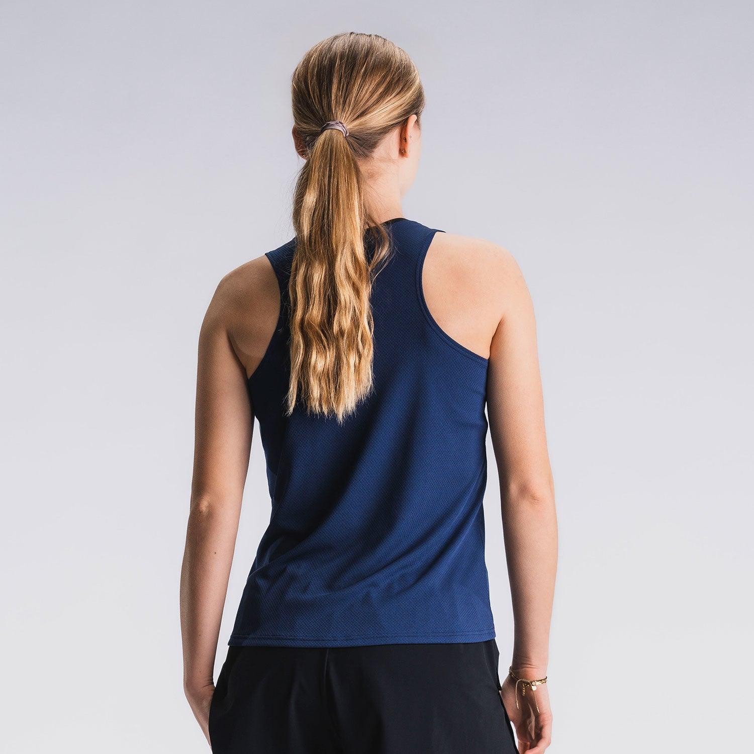 Vrouw in blauw hardlooptop en zwarte hardloopshorts, achteraanzicht, lichtgrijze achtergrond