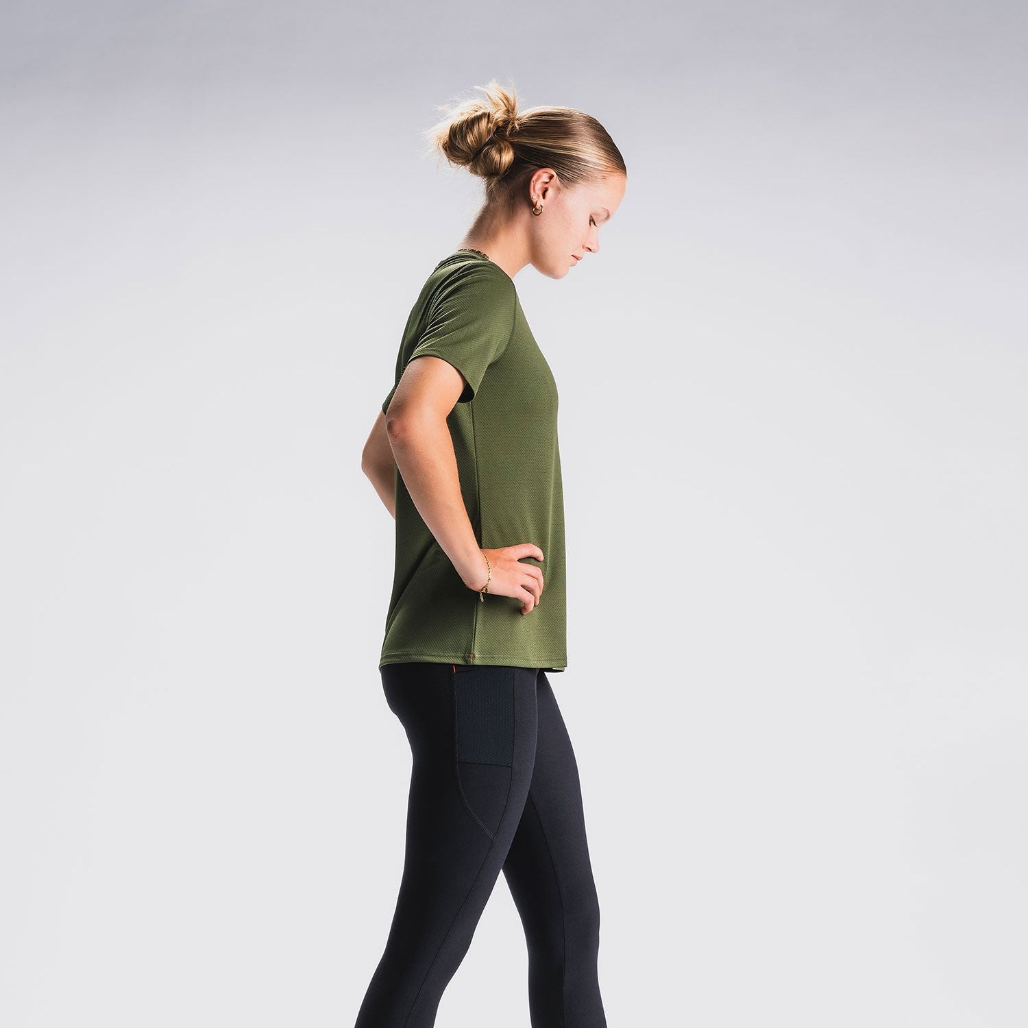Vrouw in groen sporttop en zwarte hardlooptight, zijaanzicht, witte achtergrond