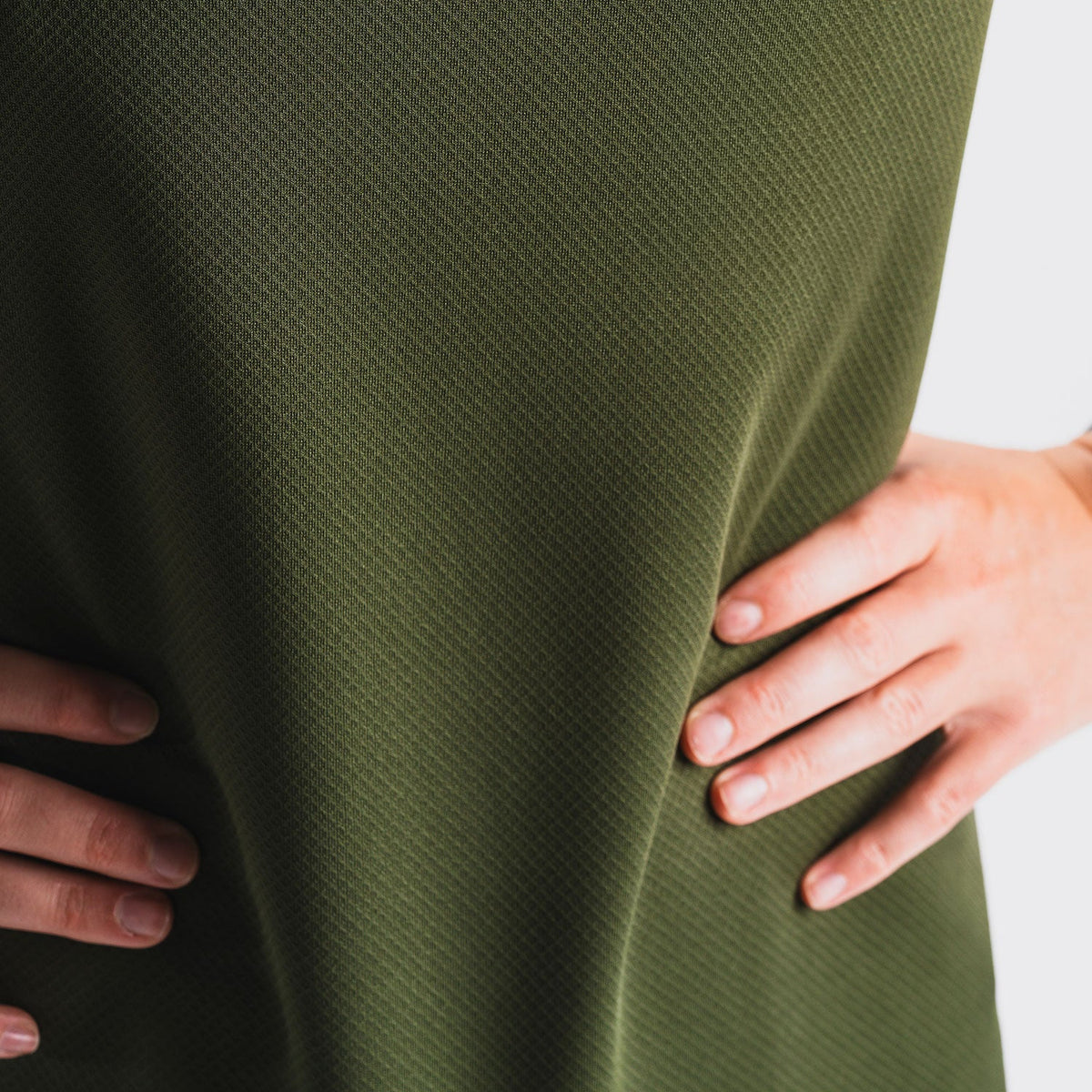 Close-up van vrouw in groen hardloop-T-shirt met ademend materiaal, handen op heupen, witte achtergrond