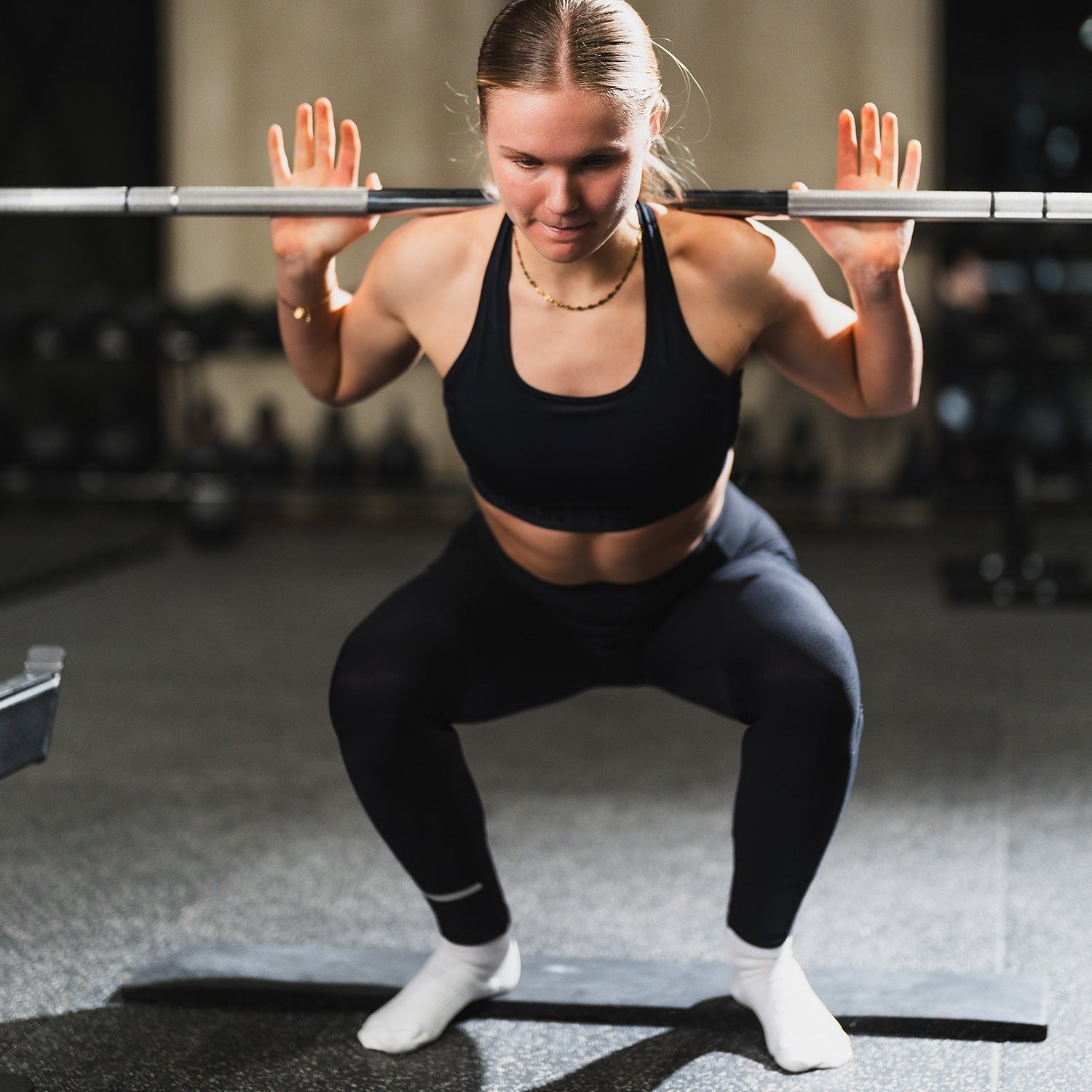 Vrouw die een squat uitvoert met een halter in een sportschool