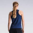 Vrouw in blauw hardlooptop en zwarte hardloopshorts, achteraanzicht, lichtgrijze achtergrond