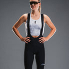 Vrouw in zwarte fietsbroek met Fusion-logo en wit fietsshirt, studiosetting, grijze achtergrond